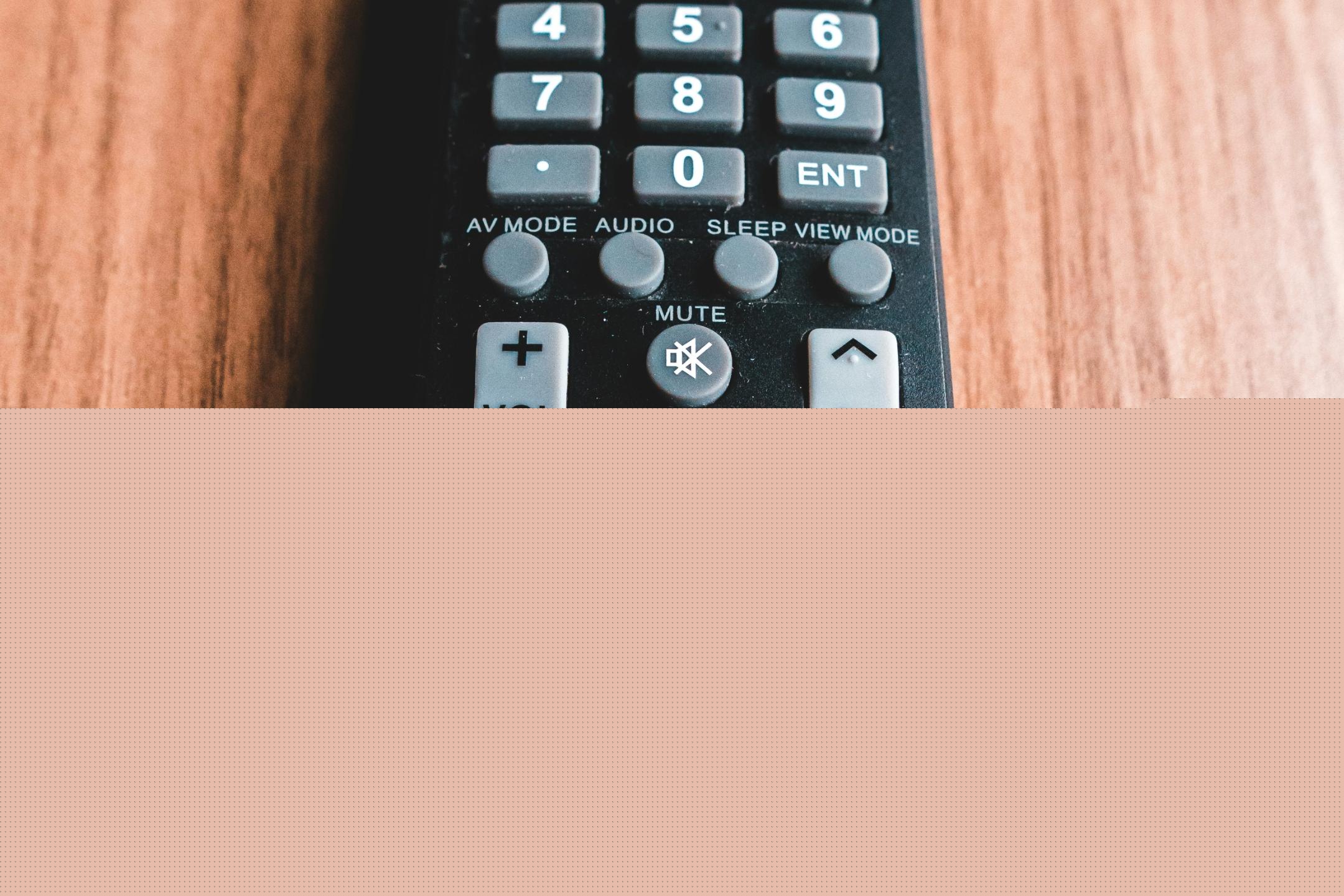 Eine schwarze Fernbedienung liegt auf einem Tischplatte.