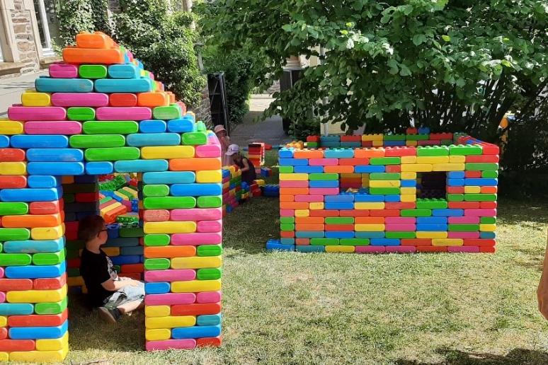 Ein KInd sitzt an einem sonnigen Tag in einem Häuschen, das aus bunten Bausteinen aus Kunststoff gebaut worden ist.